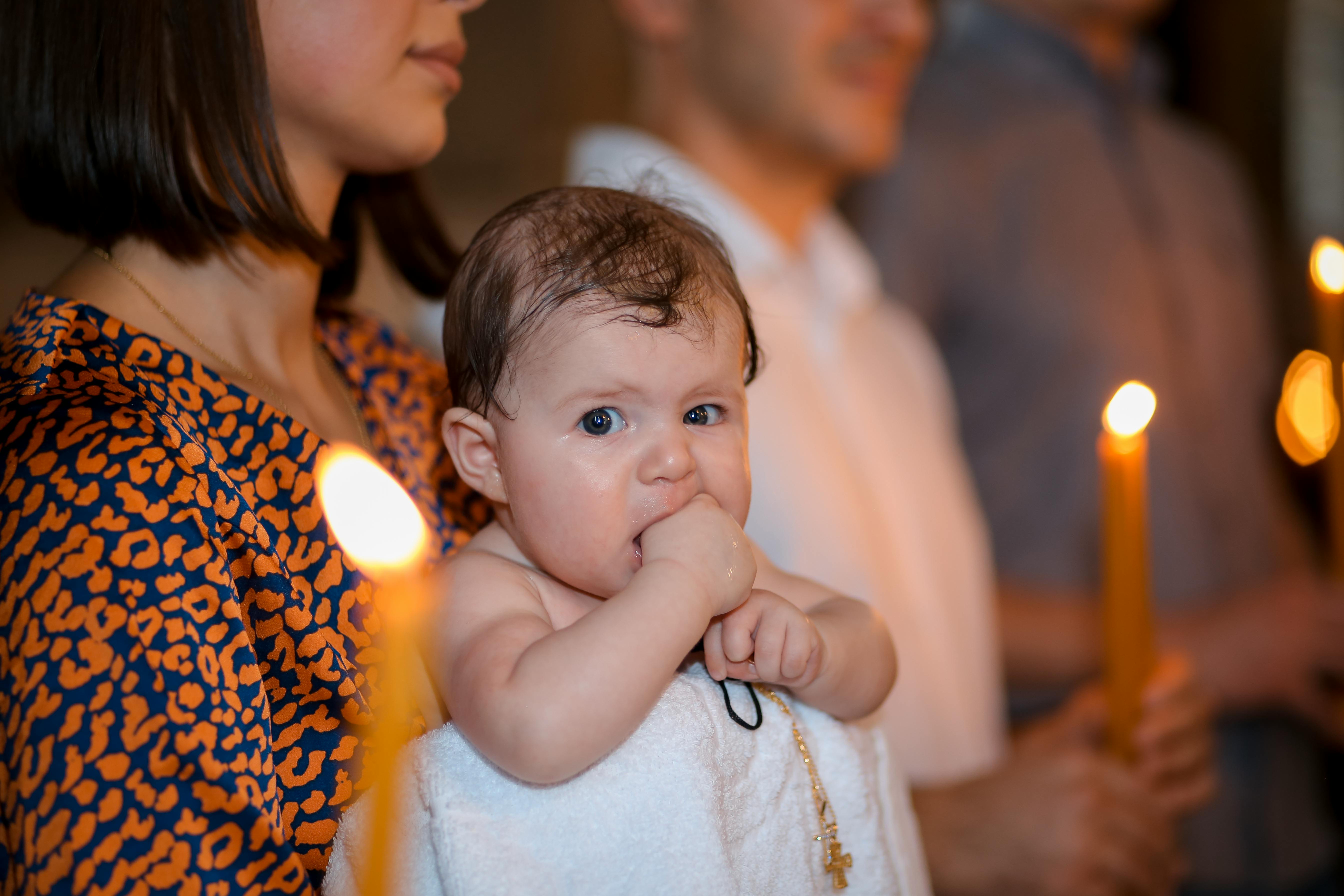 A baby held by a woman during a candlelit ceremony, evoking warmth and family bonds.