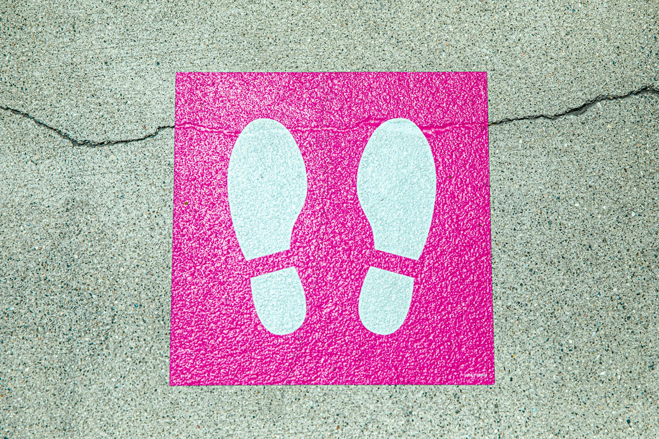 A bright pink footprint sign on a cracked concrete surface, symbolizing direction and order.