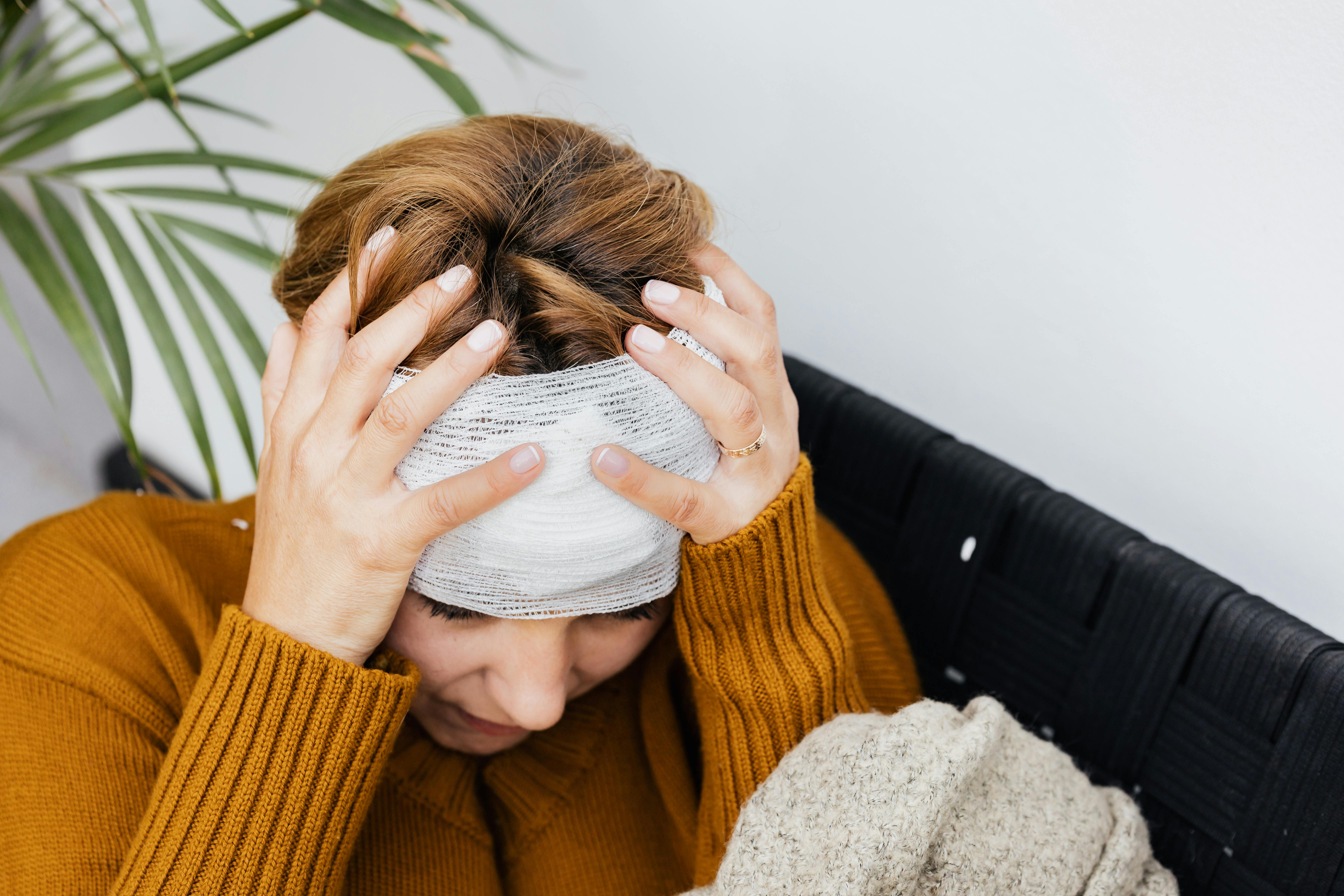 Woman with head injury holding her head in pain indoors.